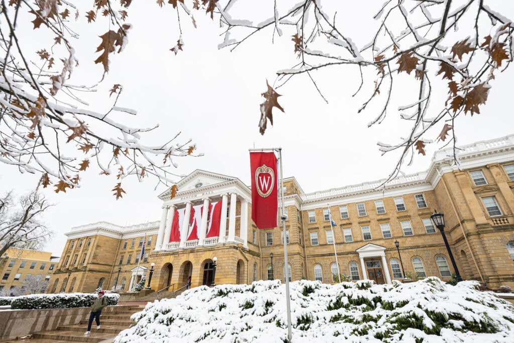 A pedestrian walks down the stairs in front of Bascom Hall as the last leaves of fall still cling to snow-covered trees following the first snow accumulation of the season at the University of Wisconsin-Madison on Nov. 16, 2022. (Photo by Bryce Richter / UW–Madison)